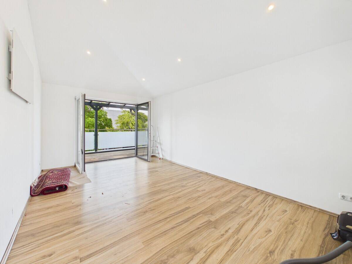 Geräumiger, heller Raum mit Holzboden und direktem Zugang zu einem überdachten Balkon.