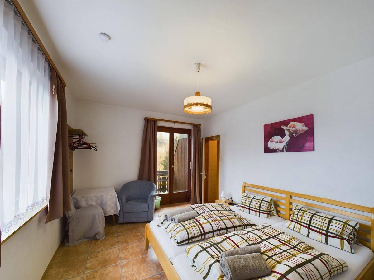 Schlafzimmer mit Doppelbett, Zugang zum Balkon und hellen Fliesenboden.