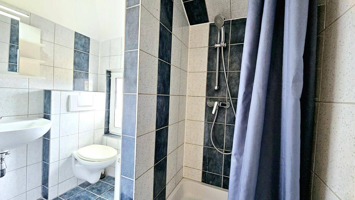 Funktionales Badezimmer mit Waschbecken, Toilette und Duschbereich in hellen Fliesen.