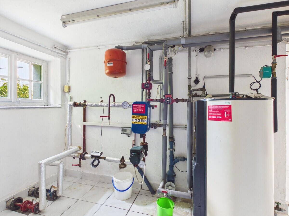 Heizungsraum mit Warmwasserspeicher, Rohren und einem Fenster.
