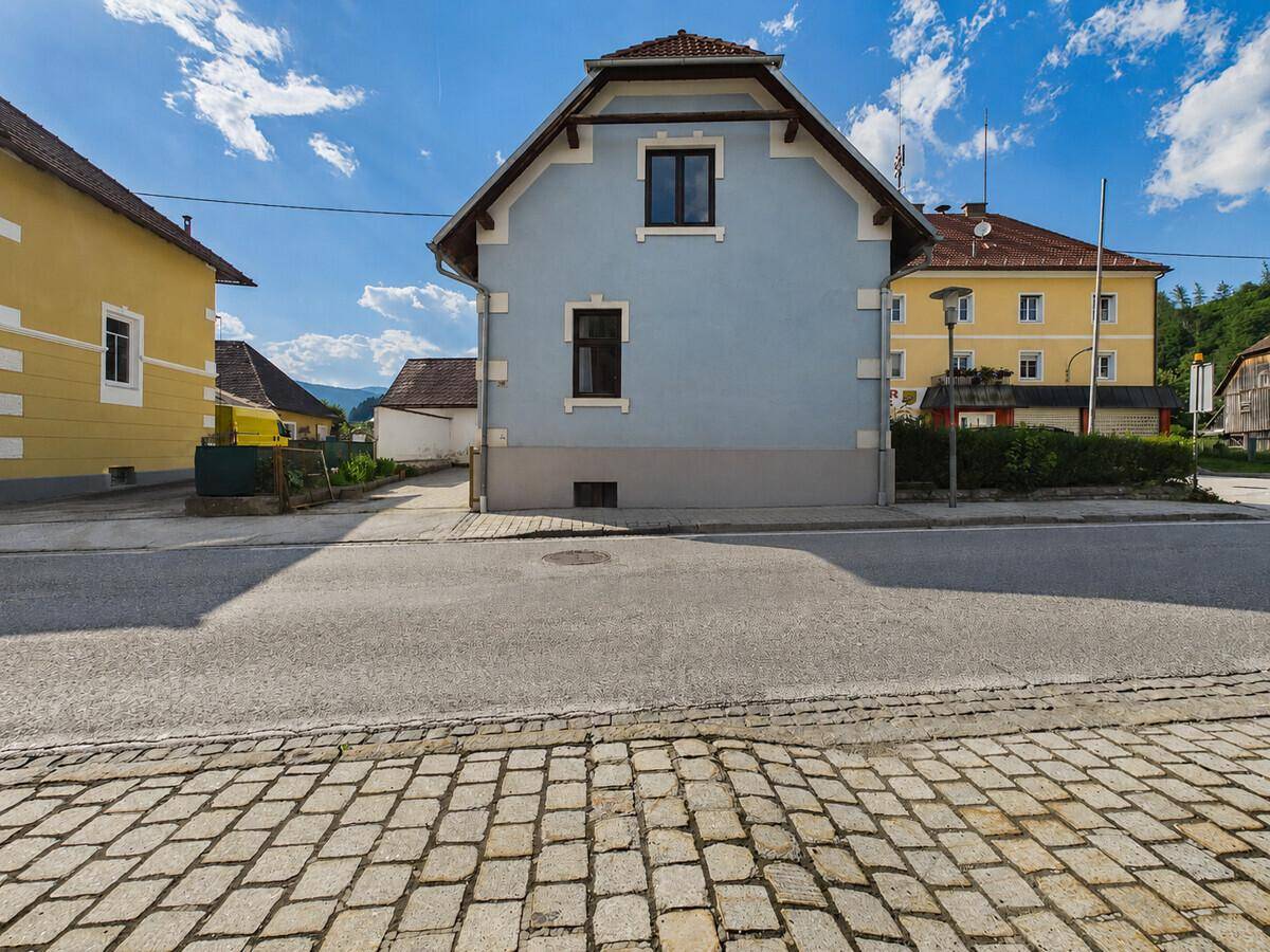 Seitenansicht des Hauses von der Straße mit Kopfsteinpflaster und blauer Fassade.