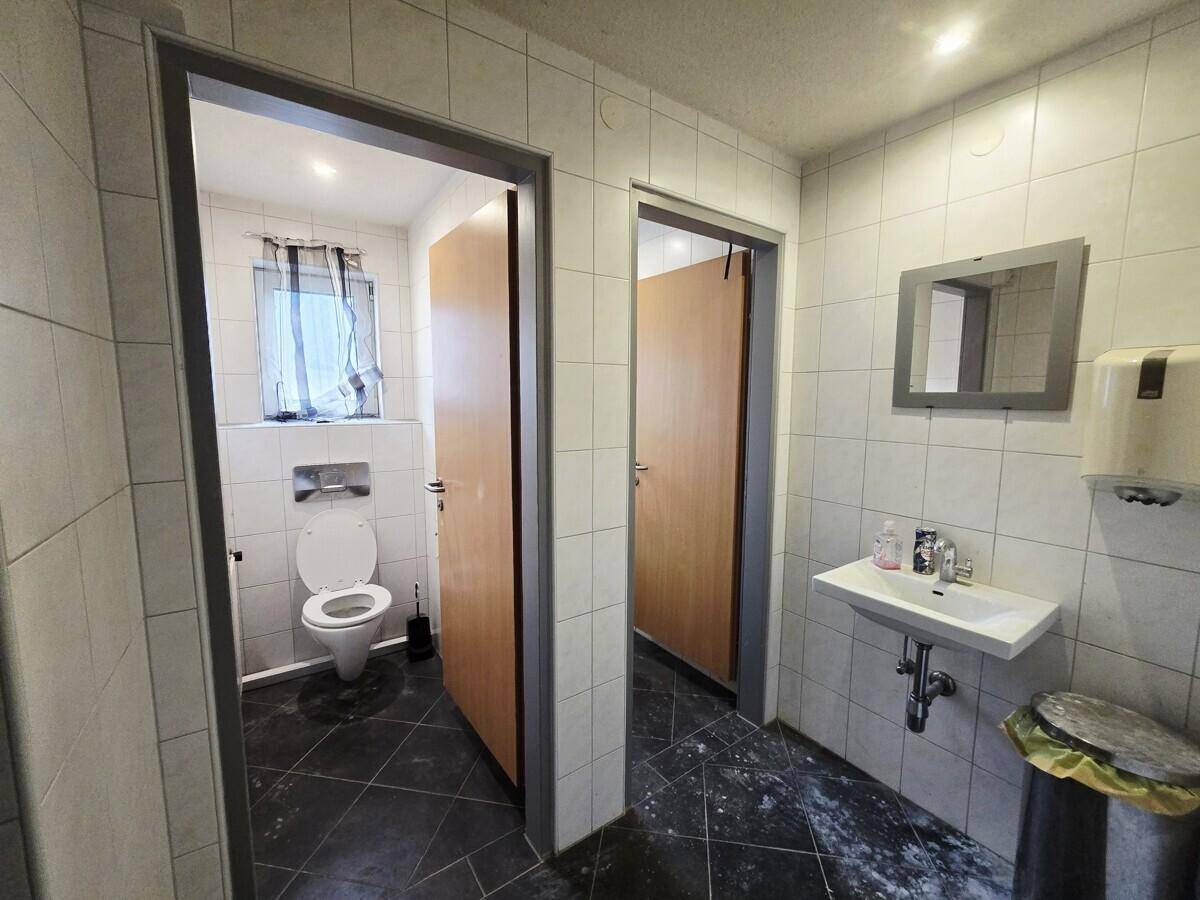 Toilettenbereich mit zwei Kabinen, einem Waschbecken und weißen Fliesen an den Wänden.