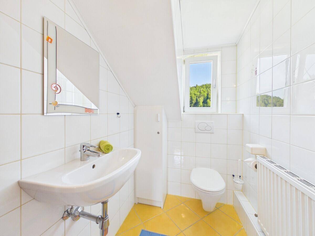 Helles WC im Dachgeschoss mit Waschbecken, Toilette und Fenster mit Waldblick.