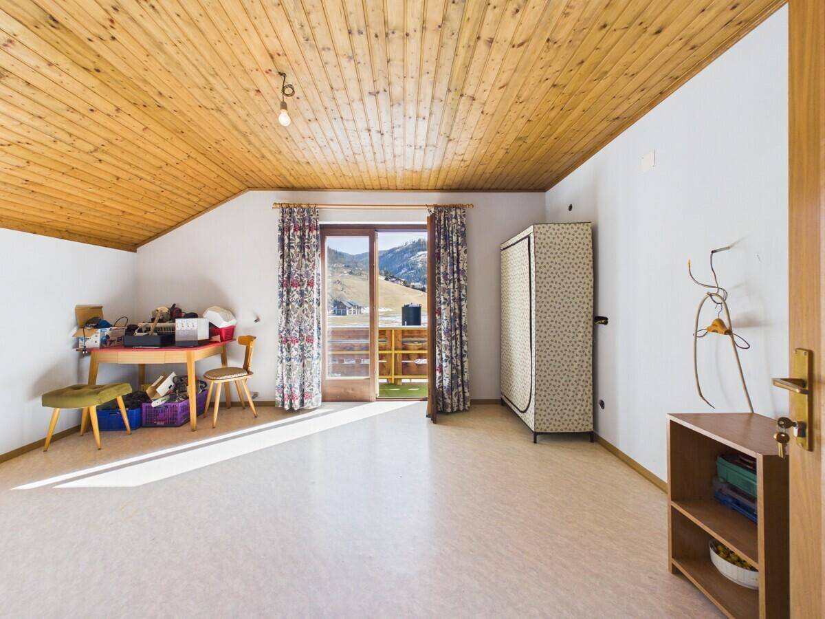 Helles Zimmer im Dachgeschoss mit Holzdecke, Schreibtisch und Zugang zu einem Balkon mit Bergblick.