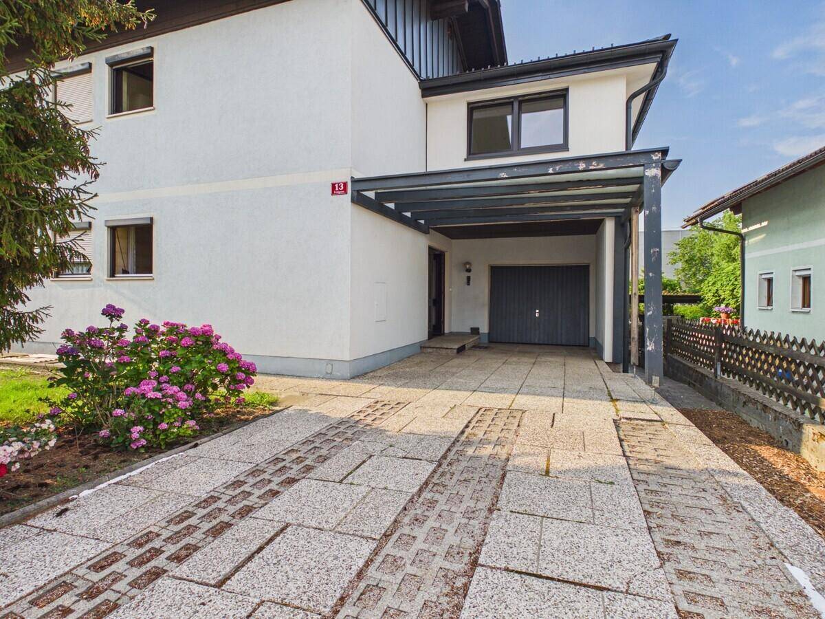 Einfahrt zum Haus mit gepflastertem Bereich, Carport und Garagentor.