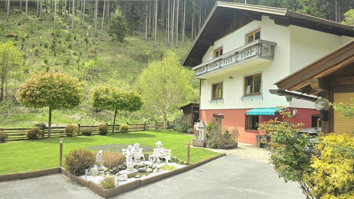 Gepflegtes Haus mit Garten, Auffahrt und Blick auf den bewaldeten Berghang.
