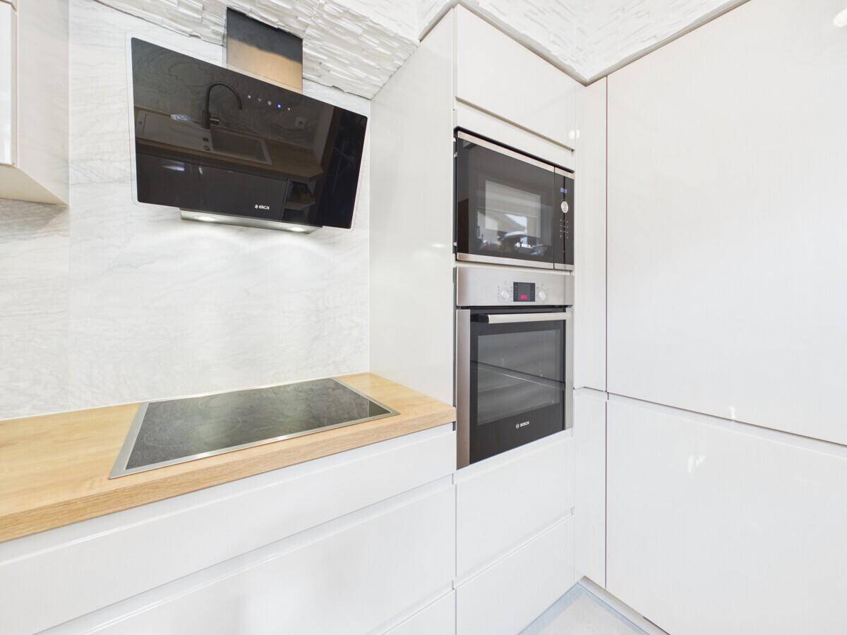 Integrierte Küchengeräte mit Backofen, Mikrowelle und Induktionskochfeld unter einer modernen Dunstabzugshaube.