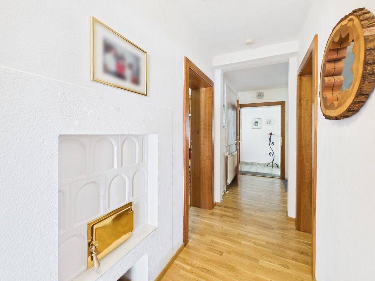 Heller Flur mit Holzfußboden, einem weißen Kachelofen und Holztüren.