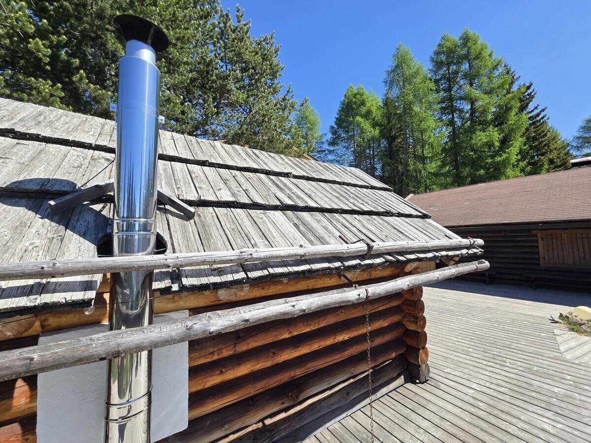 Detailansicht eines Holzhauses mit Schindeldach und modernem Edelstahlkamin.