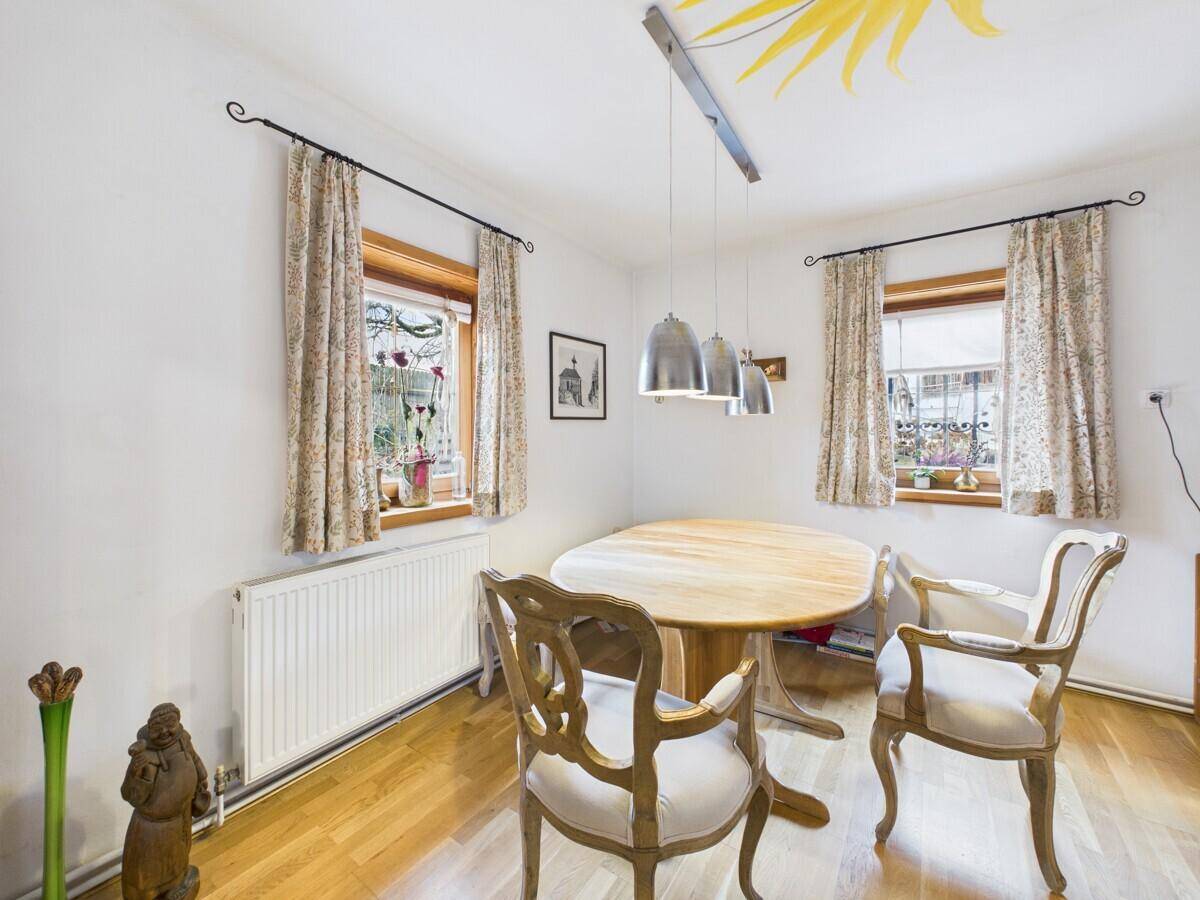 Heller Essbereich mit Holztisch, zwei Fenstern und einem dekorativen Sonnensymbol an der Decke.