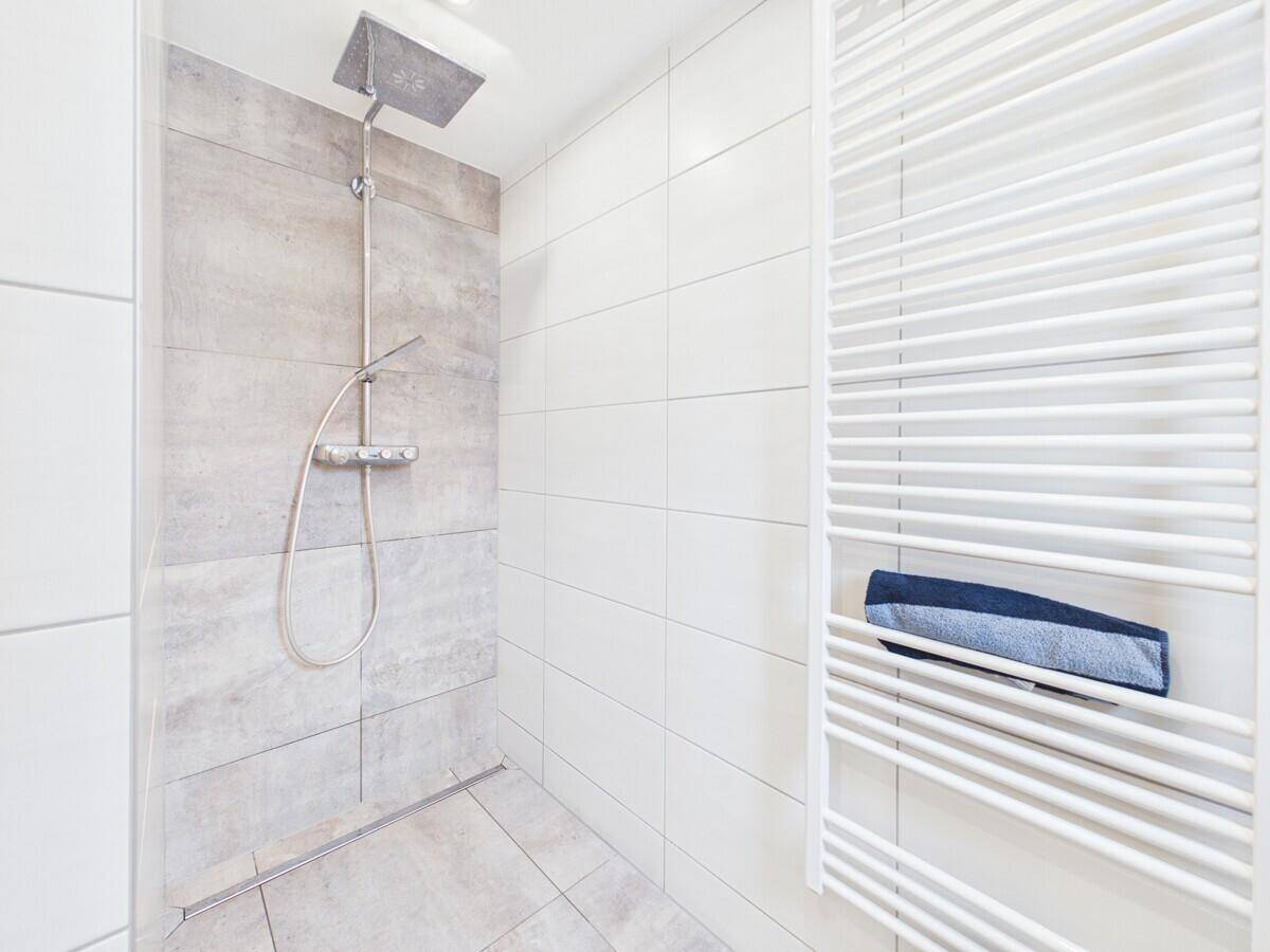 Moderne Duschkabine mit Regendusche, grauen Akzentfliesen und beheiztem Handtuchhalter.