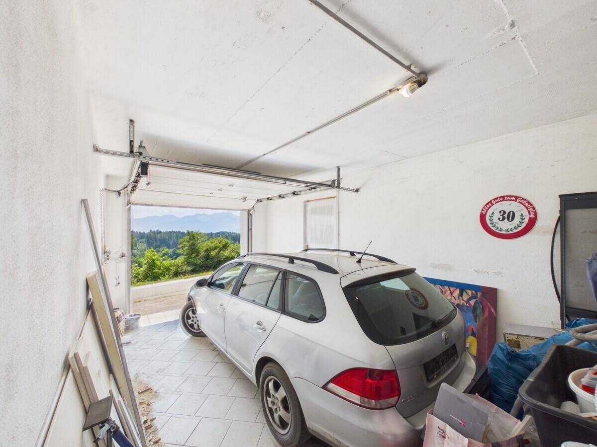 Garage mit einem geparkten Auto und geöffnetem Tor, das einen Blick auf die grüne Landschaft freigibt.