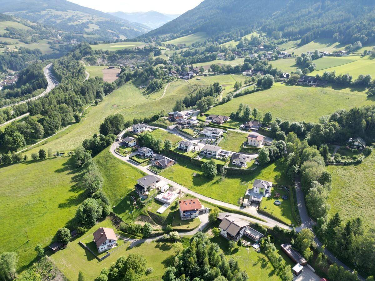 Weitläufige Luftaufnahme einer Wohngegend in einer idyllischen, grünen Hügellandschaft mit Fernblick.