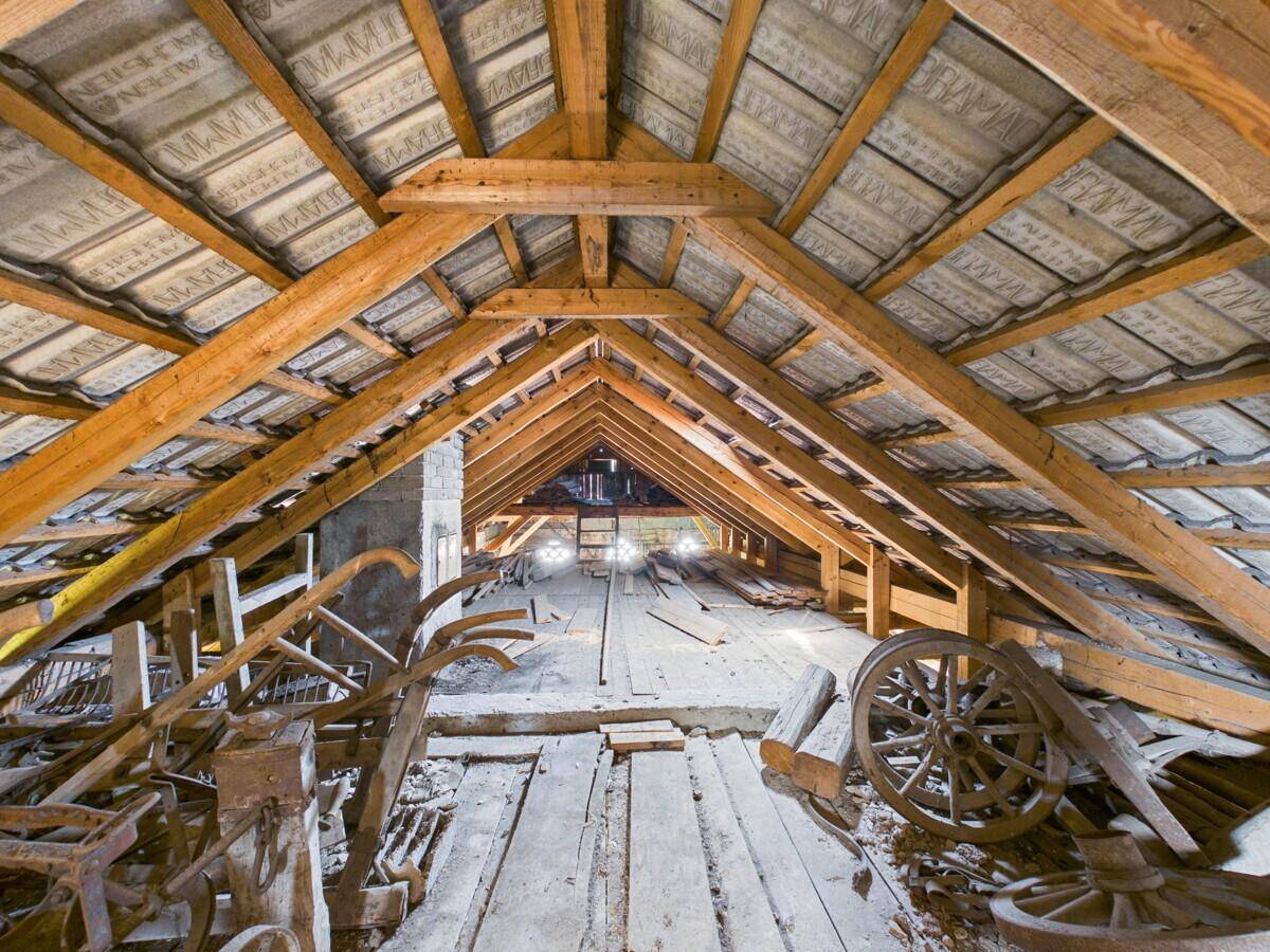 Offener Dachboden mit beeindruckender Holzkonstruktion und alten landwirtschaftlichen Geräten.