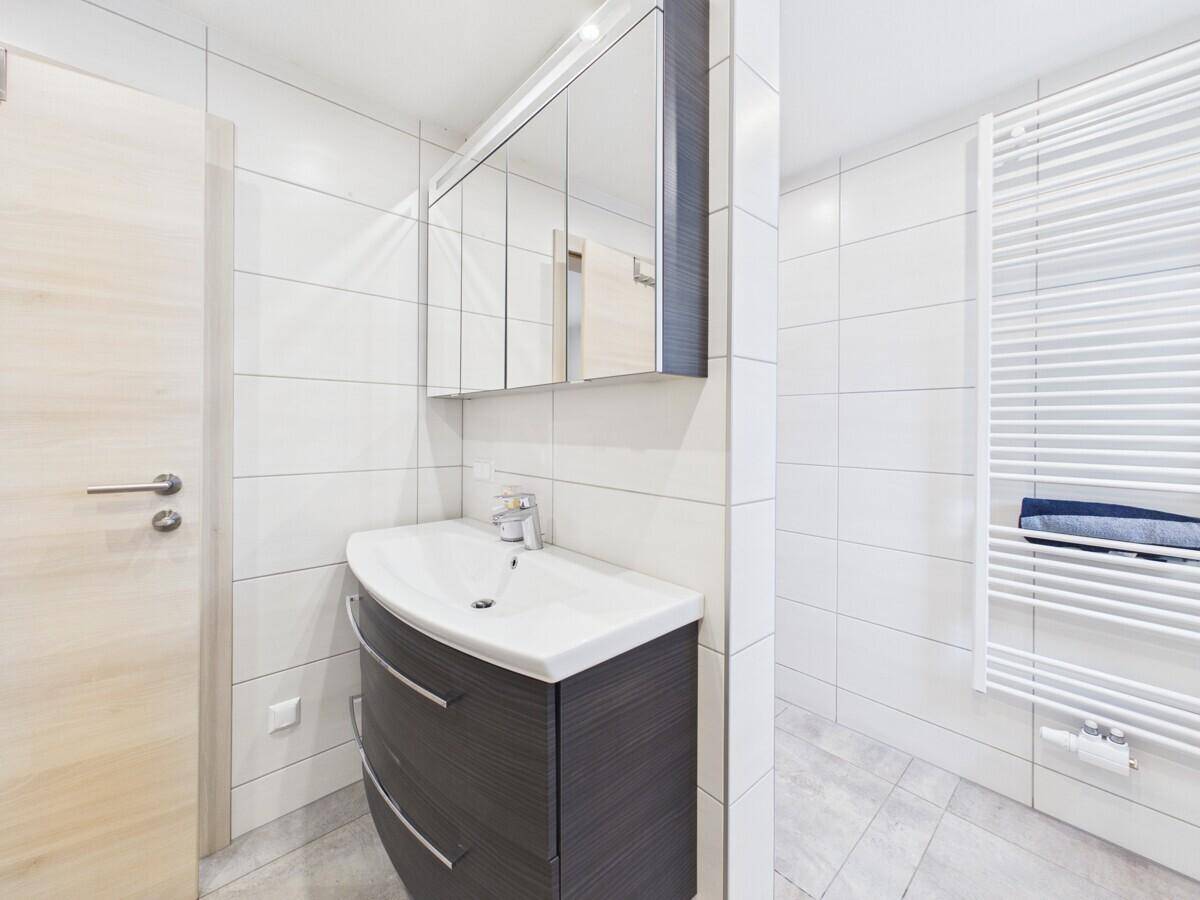 Helles Badezimmer mit modernem Waschtisch, Spiegelschrank und beheiztem Handtuchhalter.