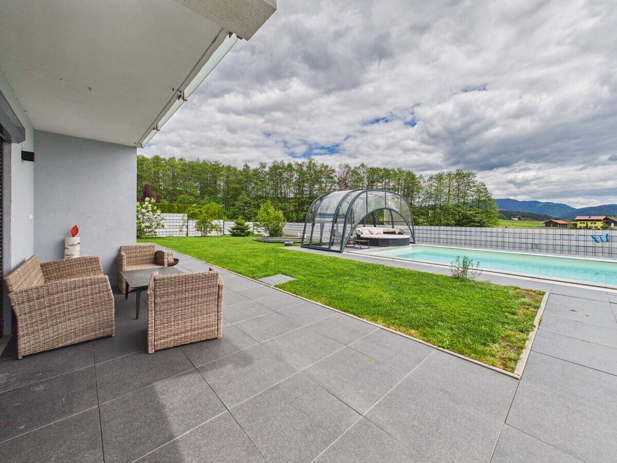 Geräumige Terrasse mit Outdoor-Sitzmöbeln und Blick auf den Garten mit Pool.