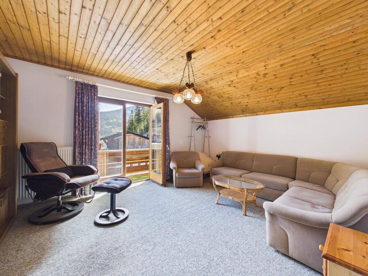 Helles Wohnzimmer im Dachgeschoss mit Holzdecke, Teppichboden und Zugang zu einem Balkon mit Bergblick.