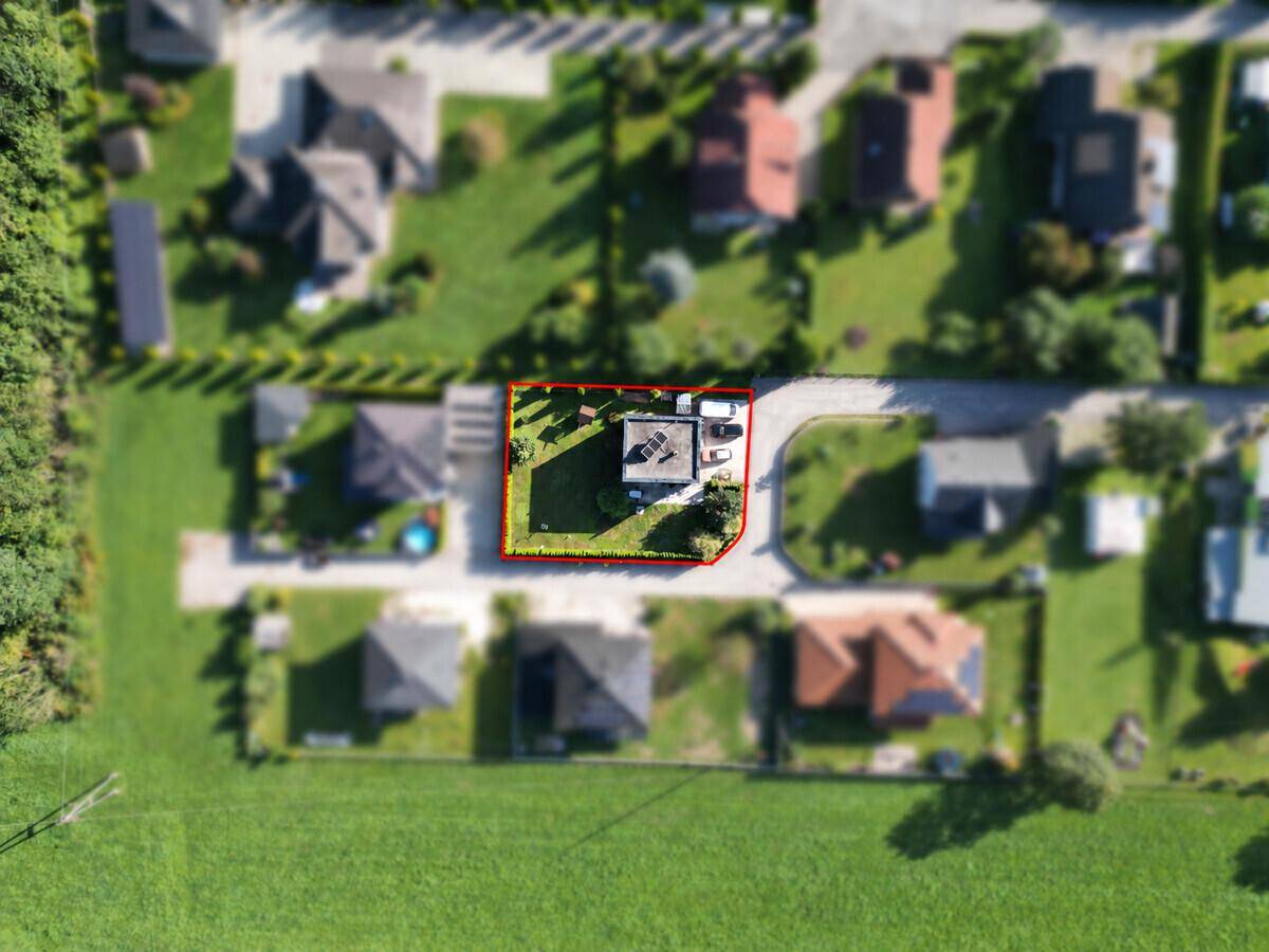Draufsicht des Grundstücks mit modernem Haus, umgeben von Rasen und Hecken.