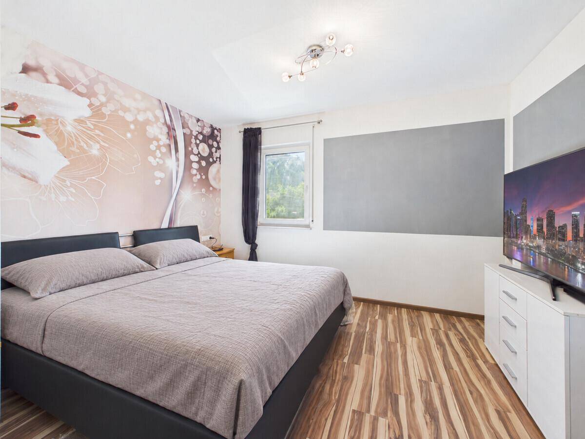 Schlafzimmer mit großem Bett, auffälliger Wandgestaltung und modernem Laminatboden.