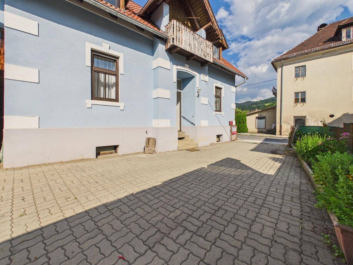 Seitenansicht des Hauses mit gepflasterter Zufahrt und sonnigem Himmel.