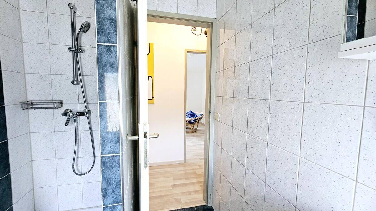 Duschbereich im Badezimmer mit weißen und blauen Fliesen, der Zugang zu einem angrenzenden Raum bietet.