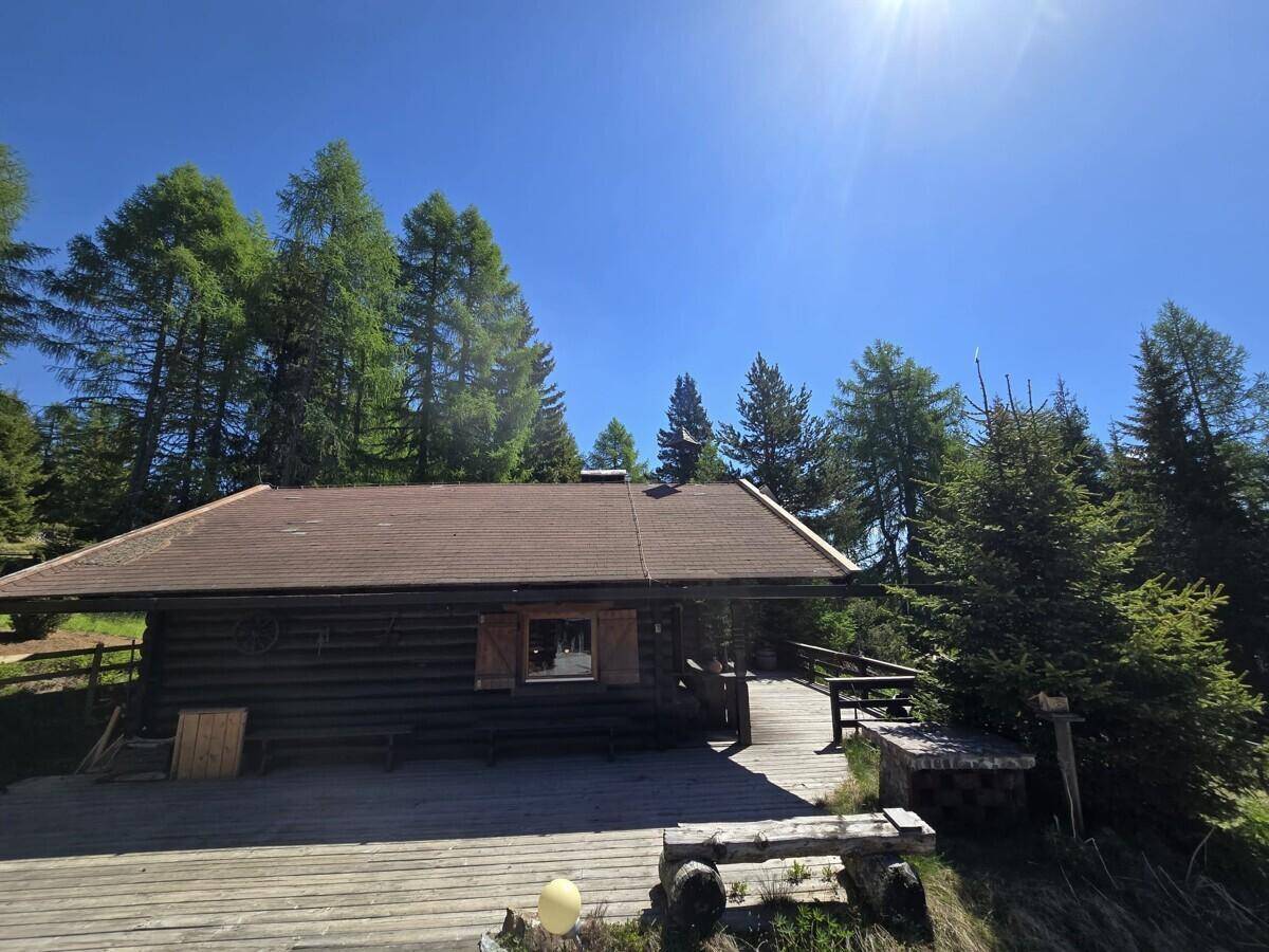 Rustikales Holzhaus mit Schindeldach und großer Holzterrasse in sonniger Lage.