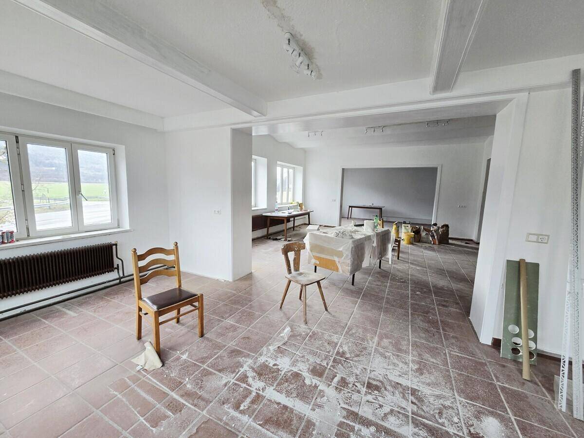 Heller Innenraum mit Fliesenboden und Renovierungsspuren, der durch seine großen Fenster viel natürliches Licht empfängt.
