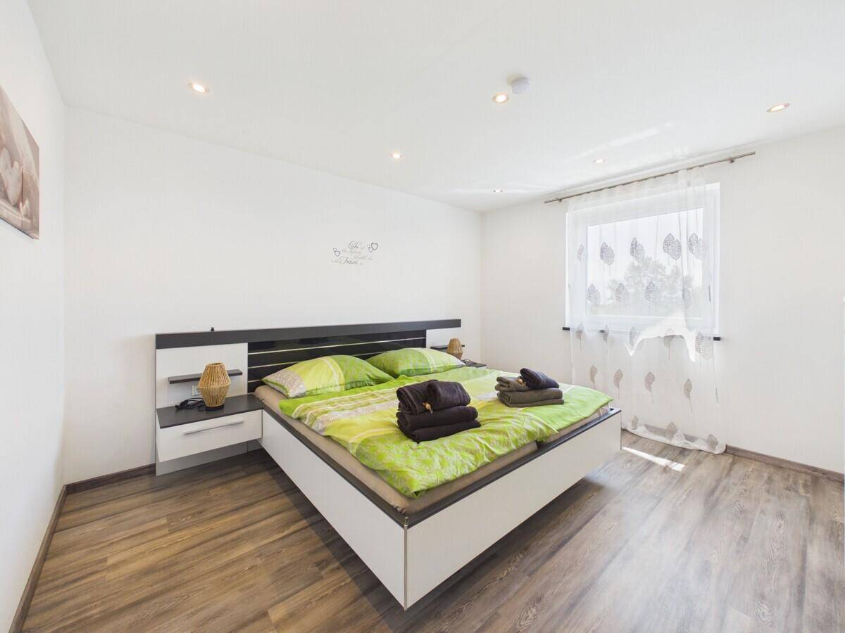 Helles Schlafzimmer mit modernem Doppelbett, Nachttischen und hellem Holzboden.