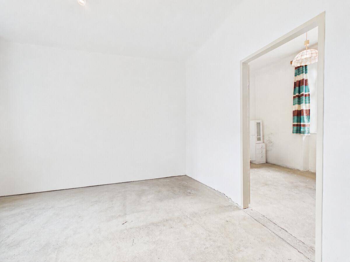 Leerer Raum mit weißen Wänden und Betonboden, bereit für die Renovierung.