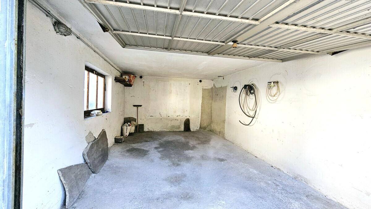 Leere Garage mit Betonboden, Fenster und Metall-Deckenkonstruktion.