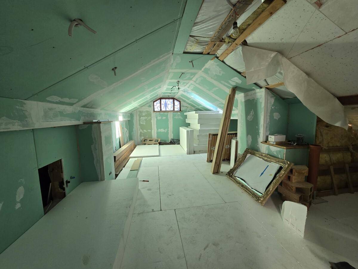 Unausgebauter Dachbodenbereich mit sichtbaren Balken und Dachfenster, bereit für den Ausbau.