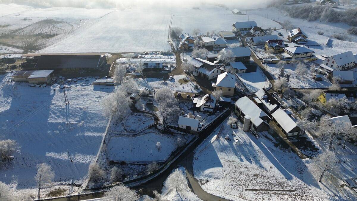 Luftaufnahme eines verschneiten Dorfes und der umliegenden Felder in einer Winterlandschaft.