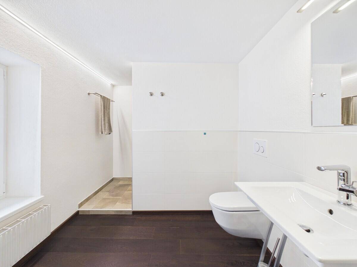 Modernes Badezimmer mit wandhängendem WC, Einzelwaschbecken und dunklem Holzboden.