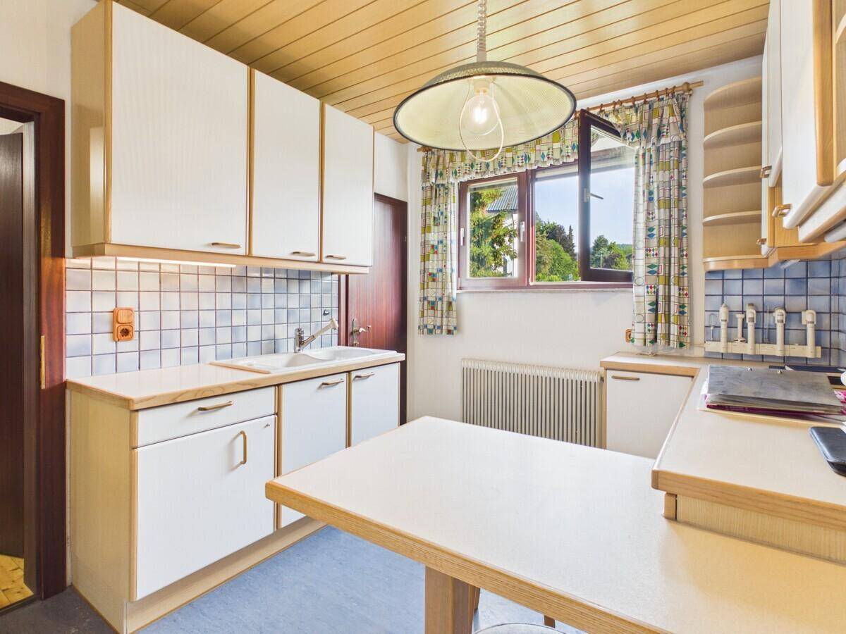 Funktionale Küche mit weißen Schränken, Holzdecke und einem Fenster mit Blick ins Grüne.