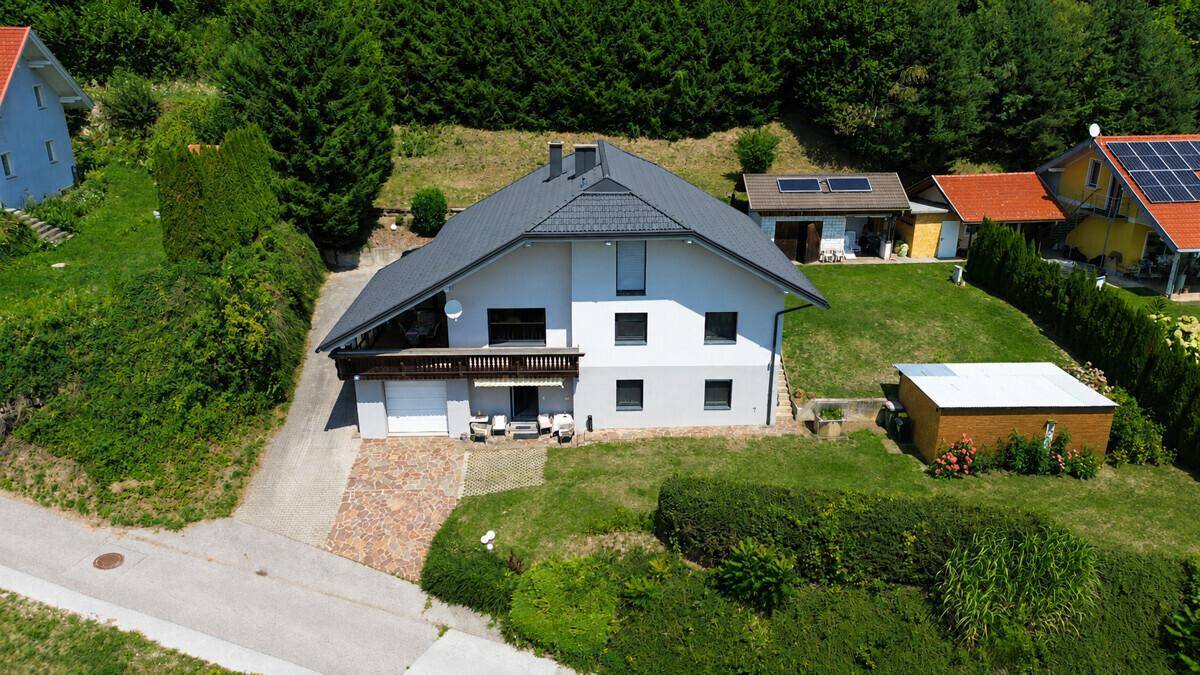 Einfamilienhaus mit Garten, Balkon und Garage, umgeben von grüner Natur und Bäumen.