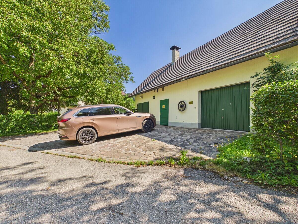 Garagengebäude mit zwei grünen Toren, gepflasterter Einfahrt und parkendem Fahrzeug.