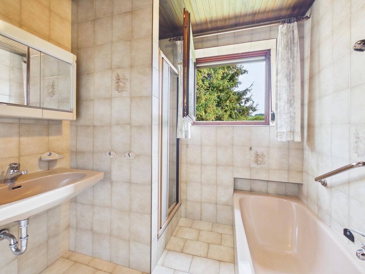 Badezimmer mit beigefarbenen Fliesen, Badewanne, Dusche und Fenster für Tageslicht.
