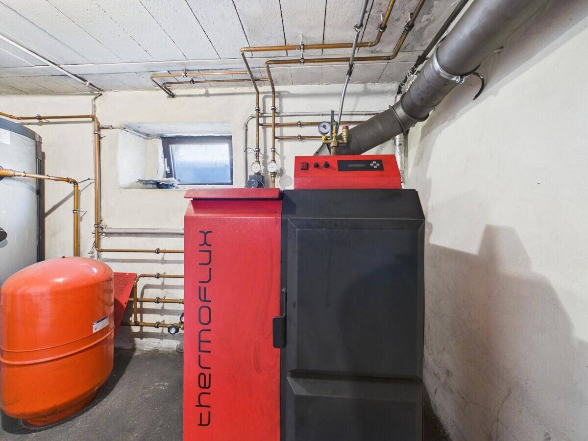 Nahaufnahme eines roten Heizkessels im Heizungsraum mit freiliegenden Kupferrohren.