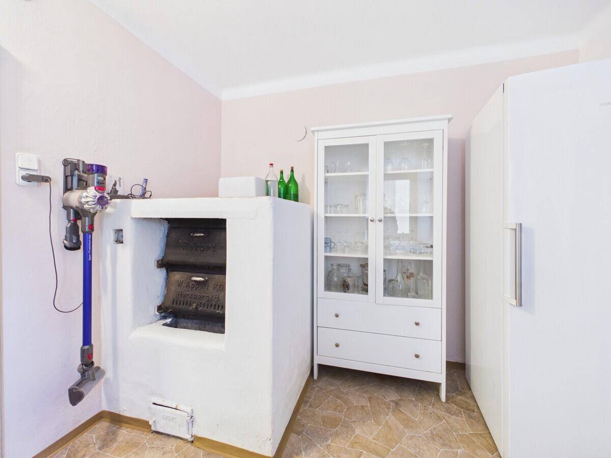 Raum mit traditionellem Kachelofen, weißem Vitrinenschrank und praktischem Fliesenboden.