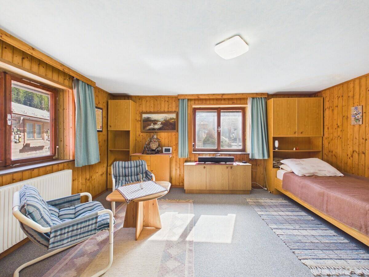 Helles Schlafzimmer mit Holzvertäfelung, Teppichboden und Fenstern mit Blick ins Grüne.
