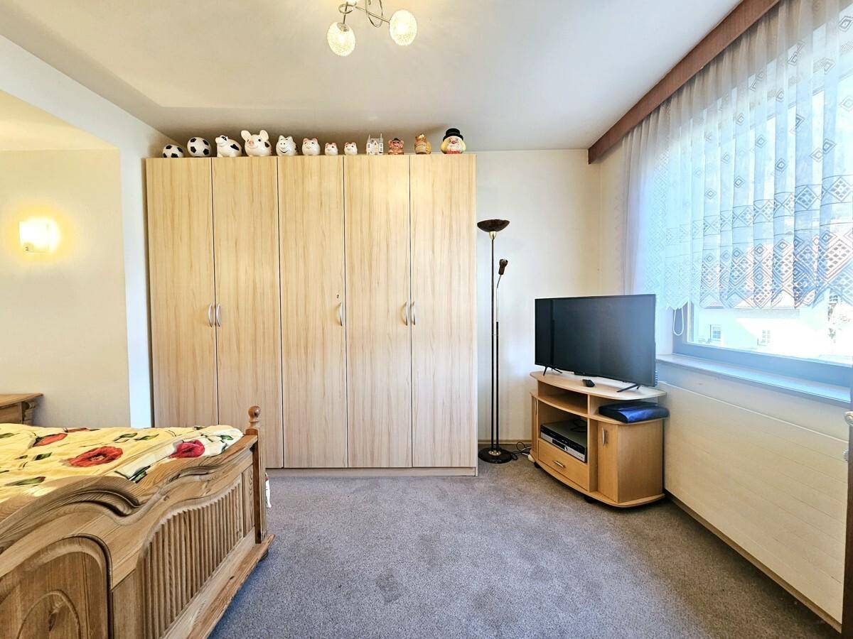 Schlafzimmer mit Teppichboden, großem Kleiderschrank und Fenster.