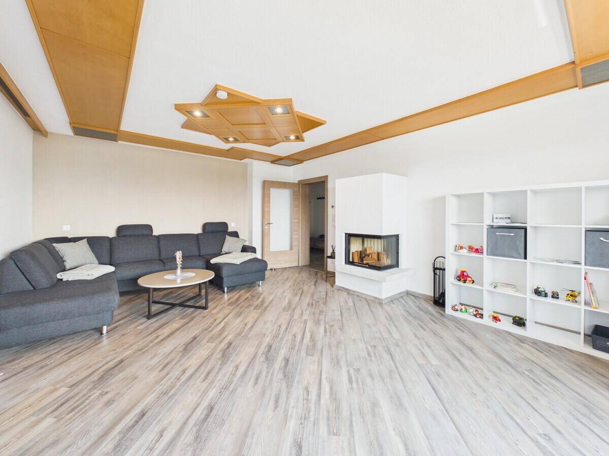 Gemütliches Wohnzimmer mit großem Ecksofa, modernem Kamin und dekorativer Holzdecke.