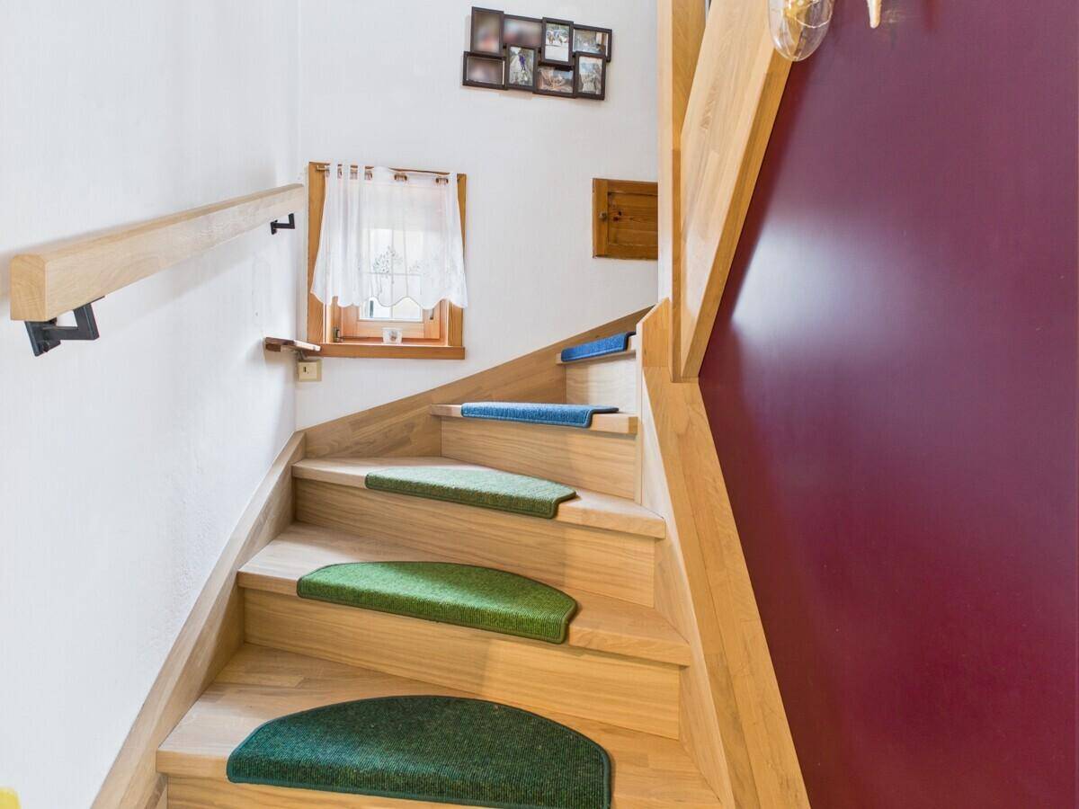 Helle Holztreppe mit grünen Teppichläufern und einem kleinen Fenster für natürliches Licht.