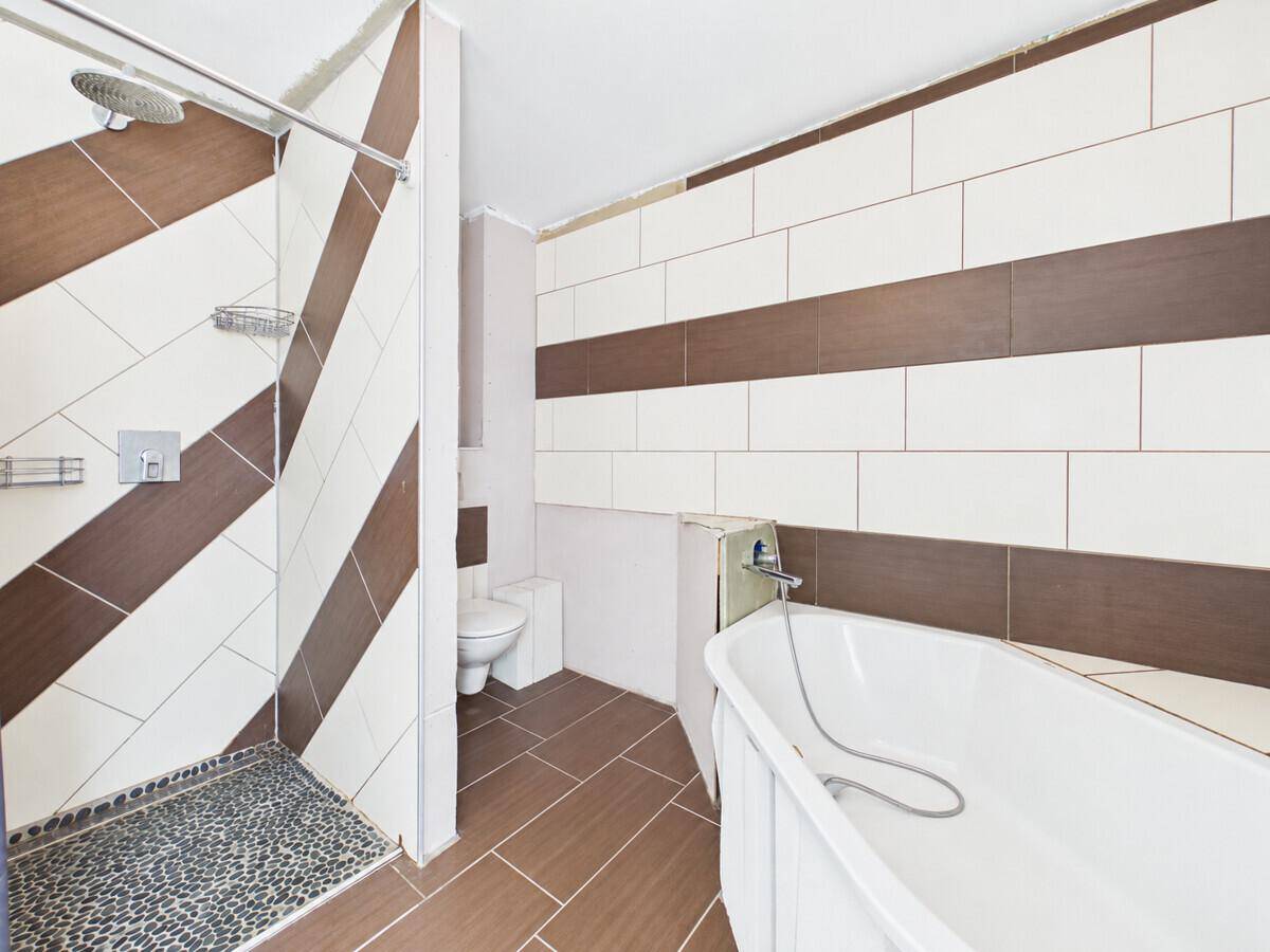Badezimmer mit braun-weißen Fliesen, Duschbereich und Badewanne.