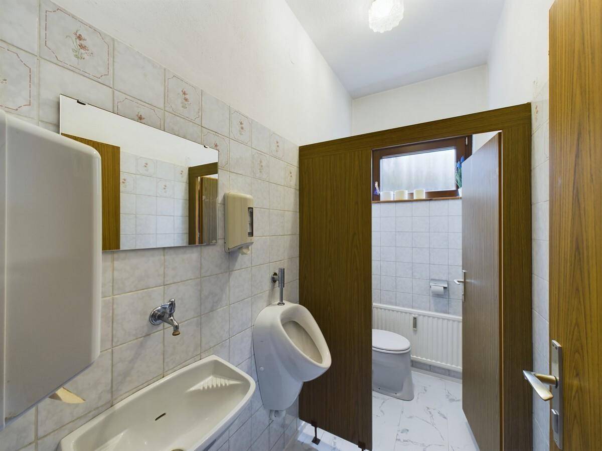 Toilettenraum mit Urinal, Waschbecken und gefliesten Wänden.