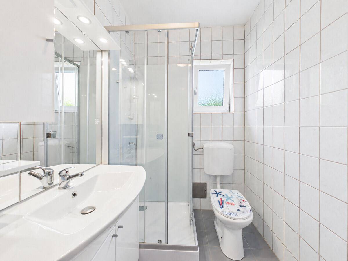 Helles Badezimmer mit weißen Fliesen, Dusche, WC und Fenster für Tageslicht.