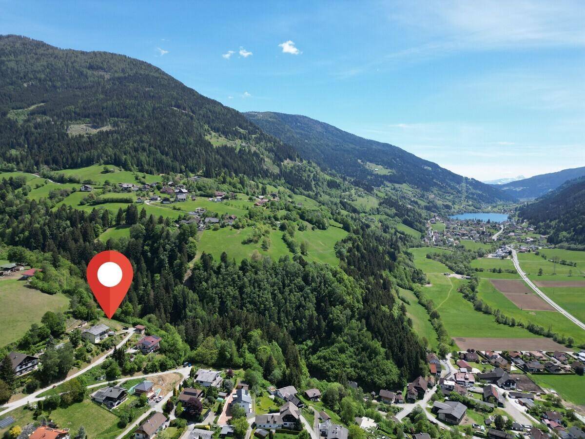 Panoramablick aus der Vogelperspektive auf ein grünes Tal mit See, Bergen und einem Dorf.