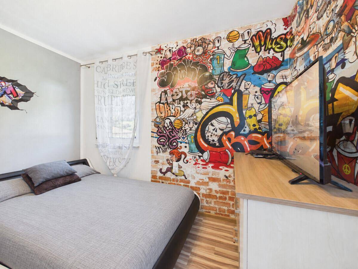 Jugendliches Schlafzimmer mit Bett, Fernseher und farbenfroher Graffiti-Tapete.