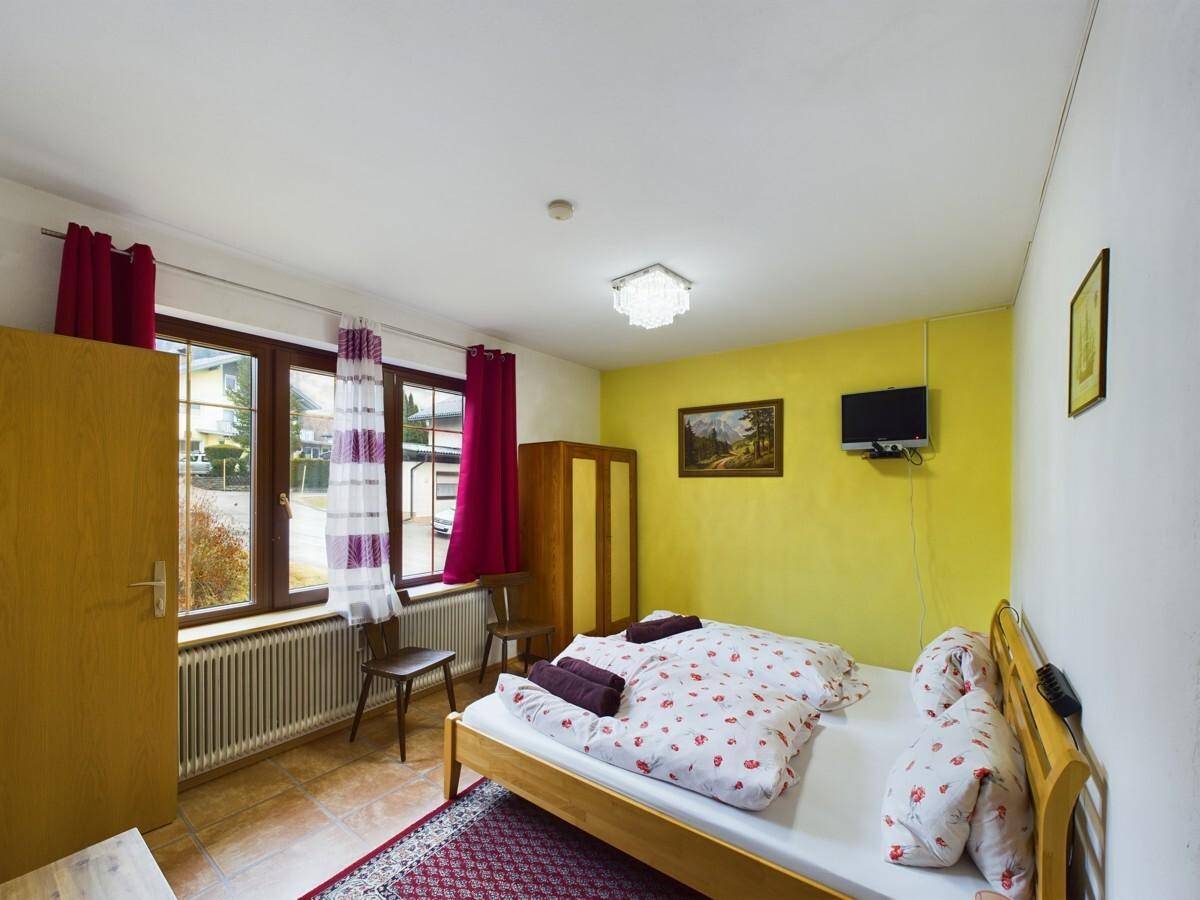 Gemütliches Schlafzimmer mit Doppelbett, gelber Akzentwand und Blick auf die Straße.