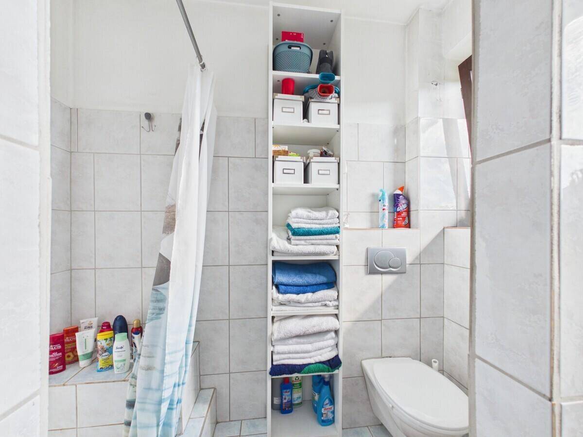 Helles Badezimmer mit Dusche, Toilette und praktischen Regalen für Handtücher.